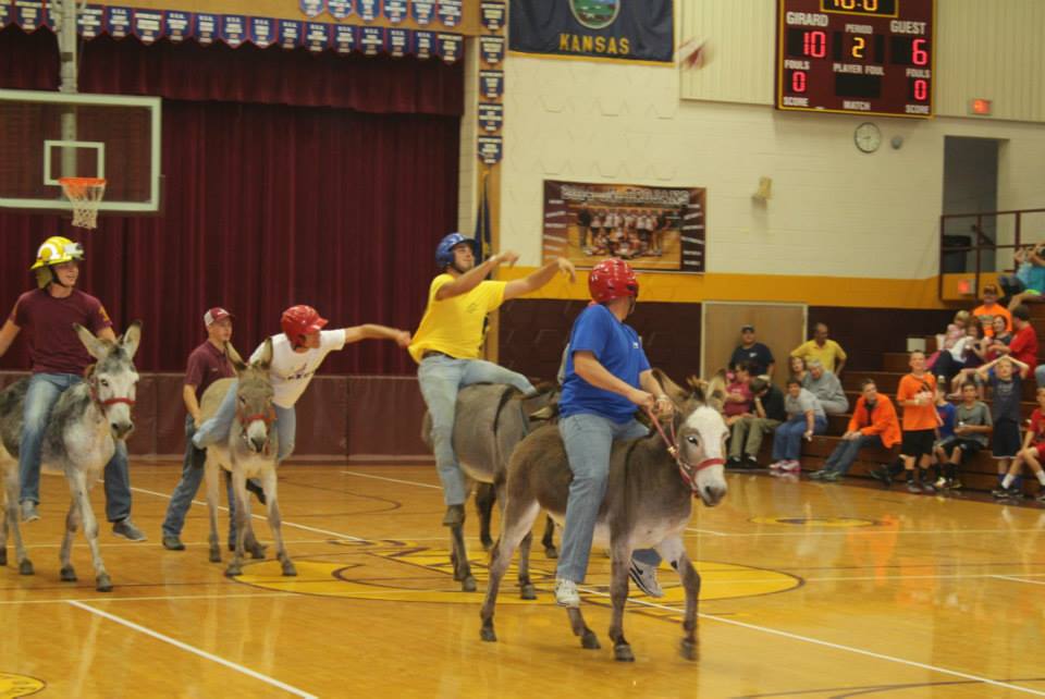 Reid shoots the basketball from his donkey while 2 people look on and another person tries to pull Reid off his donkey