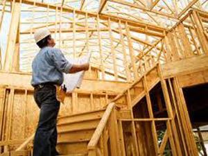 Man in wood framed building holding blue prints